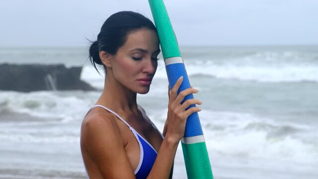 girl stands with a surfer board against the background of big waves of the ocean