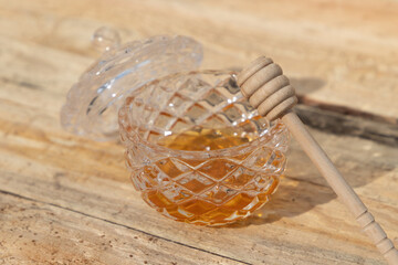 glass bowl with honey and honey dipper on a wooden table