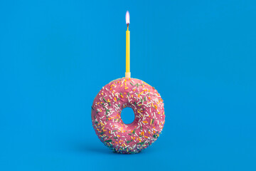food photography of sprinkled pink holiday donut front view with candle on blue background isolated...