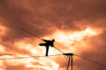Wandering tightrope walker playing on yellow sky background. Silhouette of Equilibrist businessman with pole on the rope. idea concept of help and insurance, belay in business. Show in air