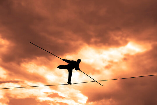 Wandering tightrope walker playing on yellow sky background. Silhouette of Equilibrist businessman with pole on the rope. idea concept of help and insurance, belay in business. Show in air