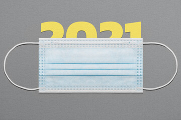Happy New Year theme card with protective mask. Paper figures 2021 under a face mask on a gray paper background. Covid-19 New Year concept in the pantone's colors of the year 2021