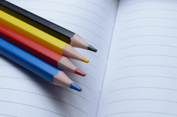 four multi-colored pencils - blue, red, yellow, black. lie on an open notebook.