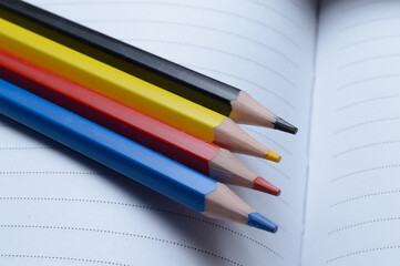 four multi-colored pencils - blue, red, yellow, black. lie on an open notebook.