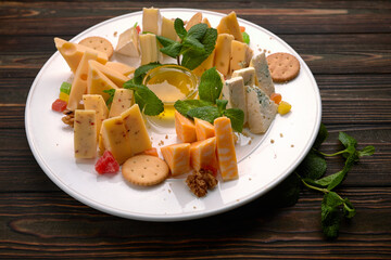 Cheese plate, assorted cheeses with mint, candied fruit, honey and cookies, on a white plate, on a dark background