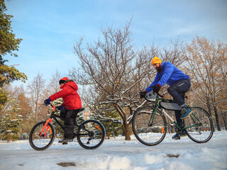 A man and his son ride bicycles in the city park in winter. An active family weekend on a sunny winter day