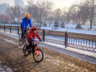 Male father and son ride bicycles on a sunny winter day. Active weekend in winter
