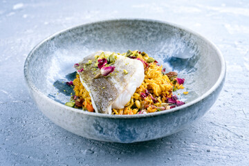 Modern style traditional sauteed skrei cod fish filet with skin in a bed of Persian jeweled saffron rice pilaw served in ceramic design bowl as close-up