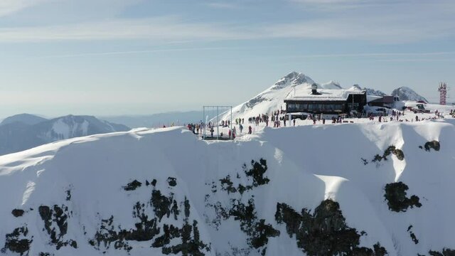 Active people spending time on mountain peak 2320 in alpine ski resort. Person enjoying extreme adventure lifestyle recreation at skiing and snowboard center reverse aerial view at sunny winter day.