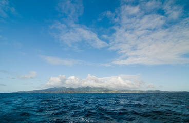 Caribbean Island on the horizon.  Deep sea with waves view over blue sky with clouds and silhouette...