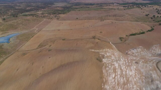 Drone top aerial panorama of a desert like hill landscape with marble stones dust at sunset in Terena near a dam lake reservoir, Portugal