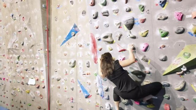 Young fit woman climbing on indoor rock wall. Aerial cinematic footage . High quality 4k footage