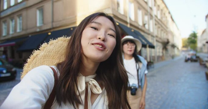POV of beautiful young Asian female making video vlog outdoors on street. Woman traveler with mother in city video chatting in good mood. Urban tourism. Close up portrait. Blogger concept