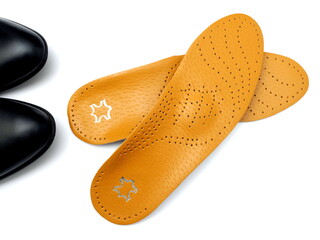 Orthopedic insoles on a white background. Treatment and prevention of flat feet and foot diseases. Foot care, comfort for the feet. Fragment Black shoes.