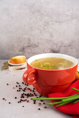 hot homemade beef bone broth with collagen and amino acids in red bowl with red napkin and green onions, black peas, chopped white onions and carrots on gray background. Concept support the immune