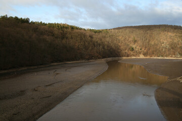 The Svratka River flows into the Brno dam. On the sides is a shore without water and a forest.