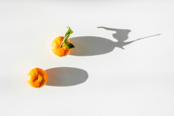 two tangerines on white table and long shadow
