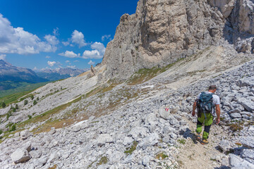 Fototapeta na wymiar Unrecognizable man walking on a hiking trail with amazing dolomite peaks background, Settsass, Dolomites, Italy