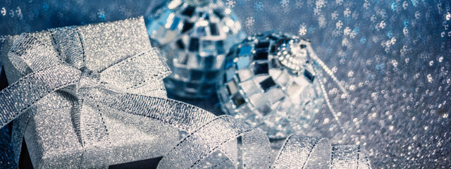 Christmas blue glittering background with sparkles and bokeh in the shape of snowflakes, a shiny gift with ribbon and bow and Christmas tree decorations balls. Festive banner with space for text.