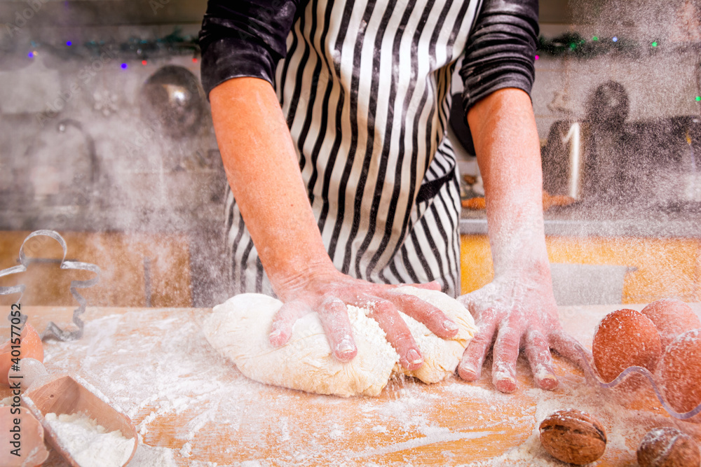 Wall mural Сloud of white flour flying into air as a woman chef energetically kneads dough on the kitchen table. Homemade non-professional cooking concept.