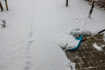 View of a person clearing snow on alley with a shovel. Winter season concept background.