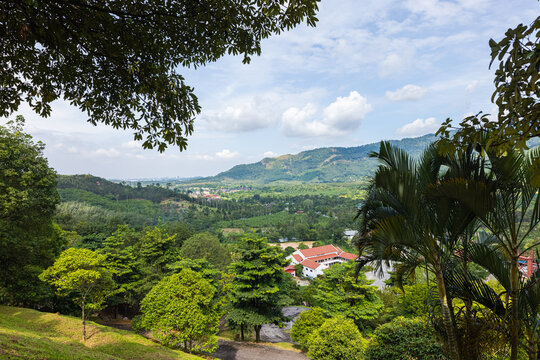 View over a valley near Broga Hill Malaysia. White clouds and blue sky. View through the trees of the forest over the valley with the small village Broga. In the background the skyline of Kuala Lumpur