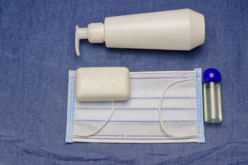 flat lay with hand sanitizer gel in spray bottle and antibacterial soap, medical mask on denim background