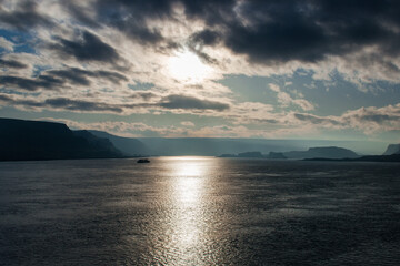 Landscape with beautiful light from the sun at noon. A landscape in gray-blue tones with a large lake reflecting the light from the sun and floating barges. A large river surrounded by blue mountains 