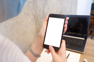 Mockup picture of business woman's hands holding smart phone with white blank screen in modern place.