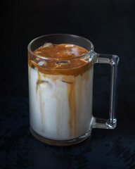 Coffee with milk and chocolate cream in a large glass mug on a black background