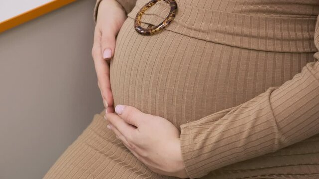 Close-up of a young pregnant woman in a brown dress sitting on a chair at a doctor's appointment