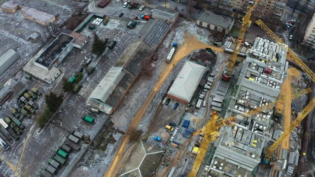 A construction site with yellow tower construction cranes - aerial drone view - concept of housing construction. Concept Investments in Housing and Business Complexes - Panning aerial Shot.