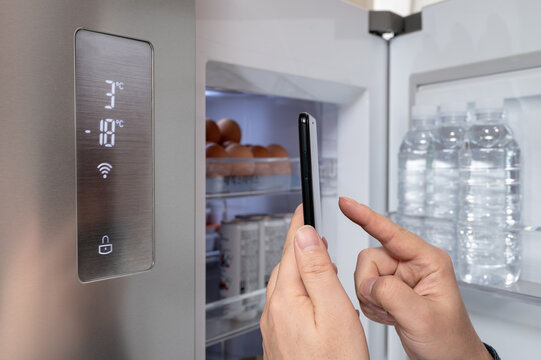 The hand of the man who controls the refrigerator with his smartphone. Internet of Things Concept.