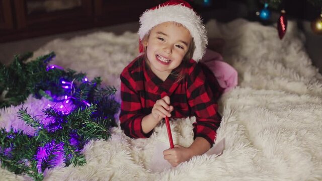 a child in red clothes is sitting waiting for the new year. the concept of celebrating Christmas at midnight. holiday costume. a girl writes a letter to Santa Claus. wish list