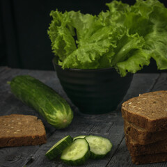 Fresh cucumbers with lettuce leaves and bread on a black wooden table.