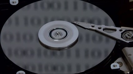 The read/write head of the actuator arm, disk platter, and spindle of a disassembled hard drive are shown spinning up, accessing data, then shutting down, with digital binary code reflecting. - Powered by Adobe