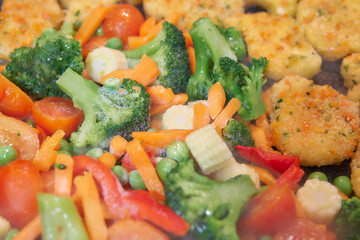Frozen vegetables and nuggets are cooked in a pan.