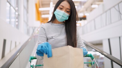 Young Asian woman in medical mask grocery walk toward camera shot, at supermarket during covid-19...
