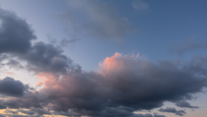 Evening sky, full screen. Lilac cumulus clouds with pink and gold backlighting against the blue sky