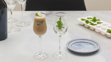 Glasses of Irish cream liquor with ice and mint leaves closeup on light grey background
