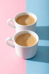 two cups of coffee on a pastel pink and blue background, photography with contrast shadow