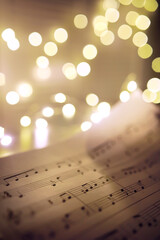 Old sheet with Christmas music notes as background against blurred lights. Christmas music concept