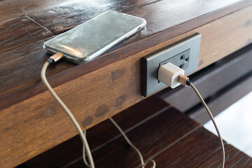 Smart phone while charging battery on wood table.