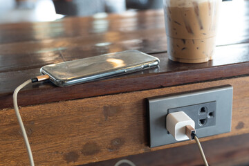 Smart phone while charging battery on wood table.