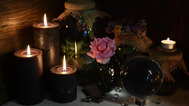 Mysterious still life with blak candles, crystal ball and rose on witch table. Esoteric, gothic and occult background with magic objects. Halloween fortune telling concept.