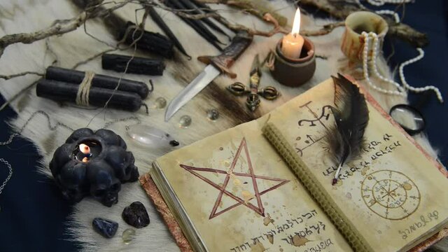 Still life with black magic grimoire book, burning candles and ritual objects on witch table. Esoteric, gothic and occult background, Halloween mystic concept.