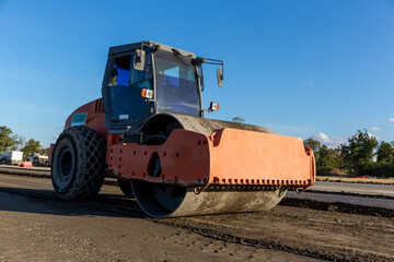 Fototapeta premium Vibratory soil compactor working on highway construction site. Tandem vibration roller compactor working on highway ground construction site. Construction of the road. Paving. Compaction of the road.