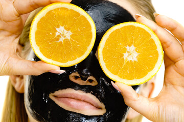 Girl black carbo mask on face holds orange fruit