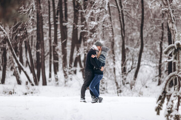 Fototapeta na wymiar The guy hugs the girl and kisses in the snowy winter forest