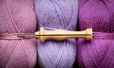 A wood punch needle tool on 3 wool balls in purple tones 